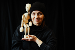Portret Marty Rau z drewniana lalką teatralną siedzącą na jej ramieniu.