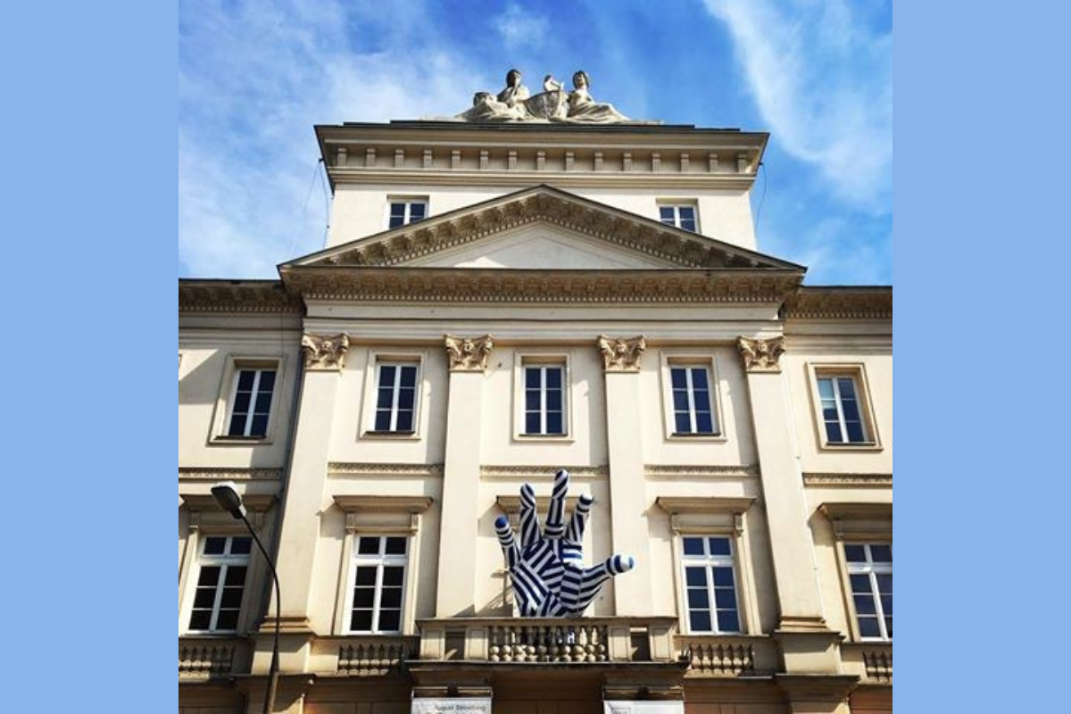 Na zdjęciu fragment fasady Akademii Teatralnej w Warszawie z widoczną charakterystyczną biało-niebieską dłonią widniejącą na balkonie.