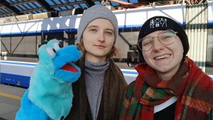 Dwie studentki na dworcu z niebieskim muppetem.