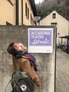 Studentka Karolina Klemczak stoi uśmiechnięta przy tablicy na murze z napisem "Accademia Teatro Dimitri".