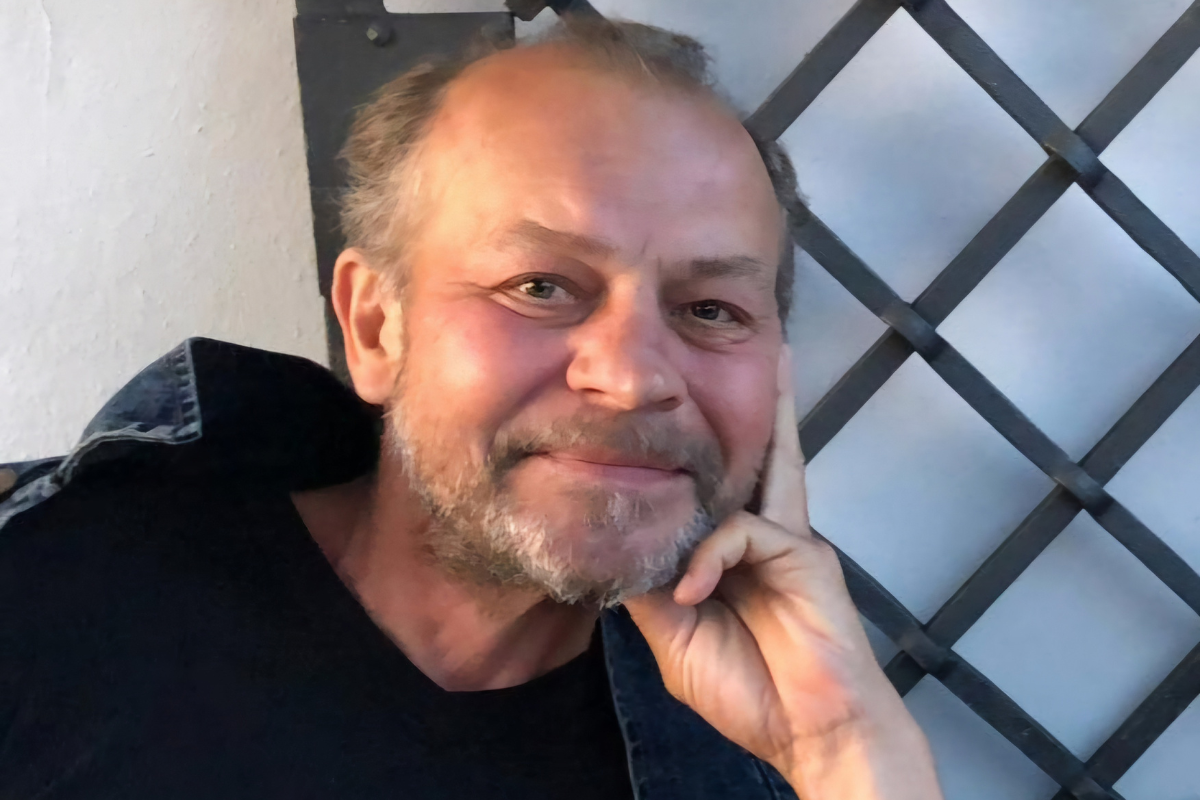 Portret uśmiechniętego Wojciecha Szelachowskiego siedzącego przy stole.