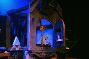 Na zdjęciu fragment odbudowanej scenografii: otwarte drewniane okienko zegara, a w nim twarz Jezusa na krzyżu i drewniana figurka psa.