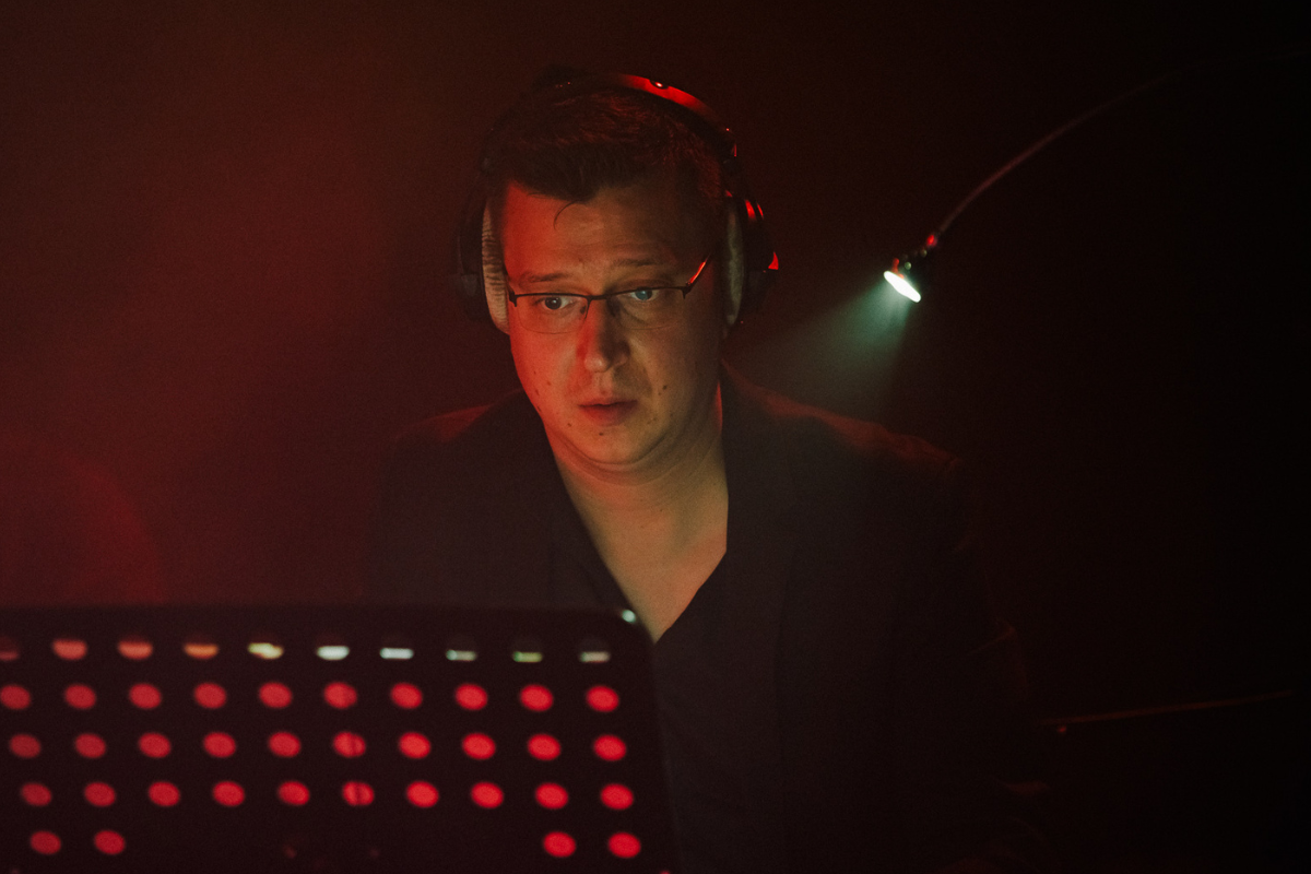 Marcin Nagnajewicz przy pracy, ze słuchawkami na uszach i w czerwonym świetle scenicznym.
