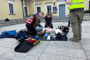 Studentka na placu miejskim reanimuje fantoma. Obok niej klęczy ratownik medyczny.