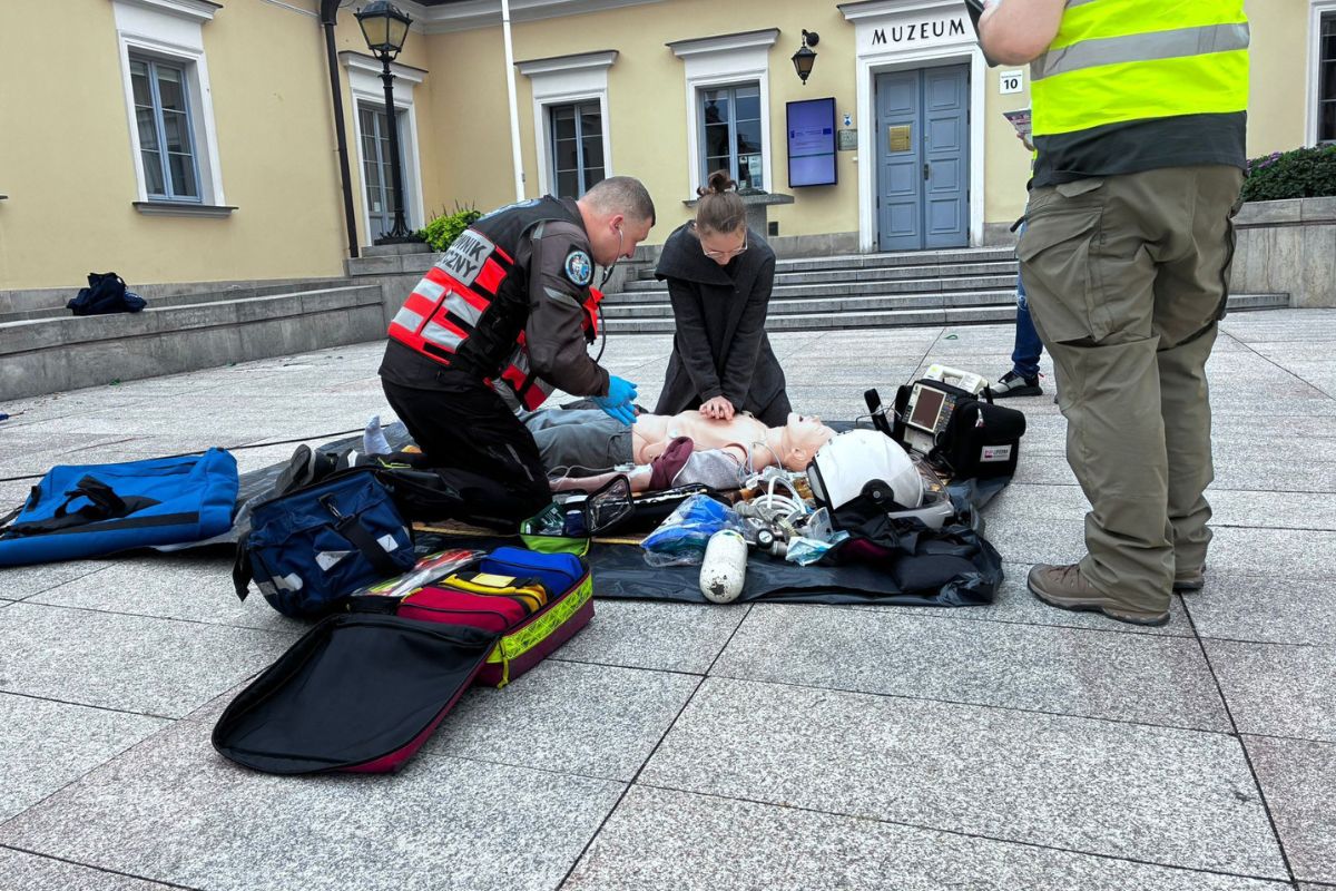 Studentka na placu miejskim reanimuje fantoma. Obok niej klęczy ratownik medyczny.