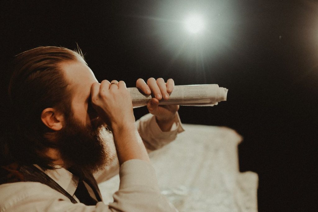 Mężczyzna patrzy przez zwiniętą gazetę niczym przez lunetę.