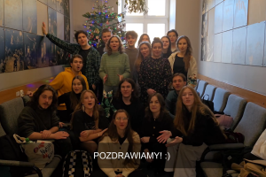 Grupa studentek i studentów pierwszego roku siedząca przy choince w korytarzu uczelni zwanym tramwajem.