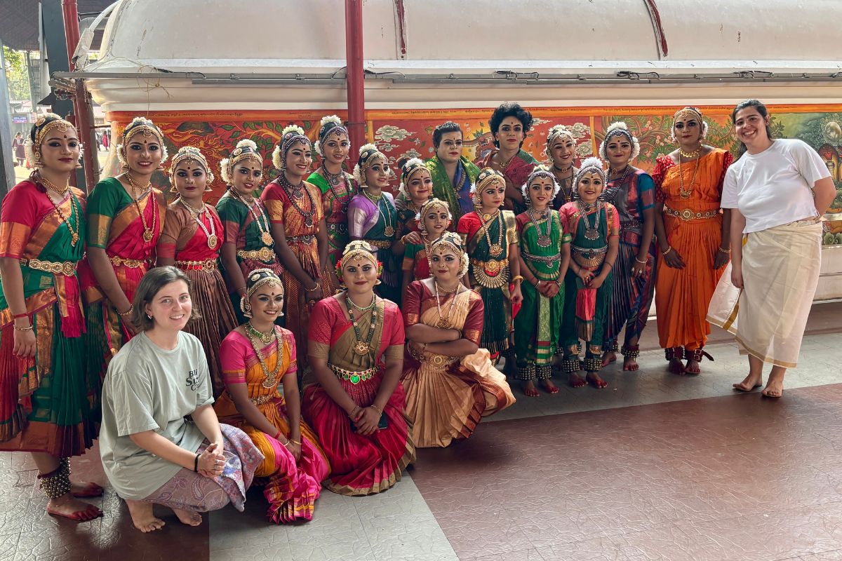 Dwie studentki pozują z dużą grupą osób w tradycyjnych indyjskich strojach.